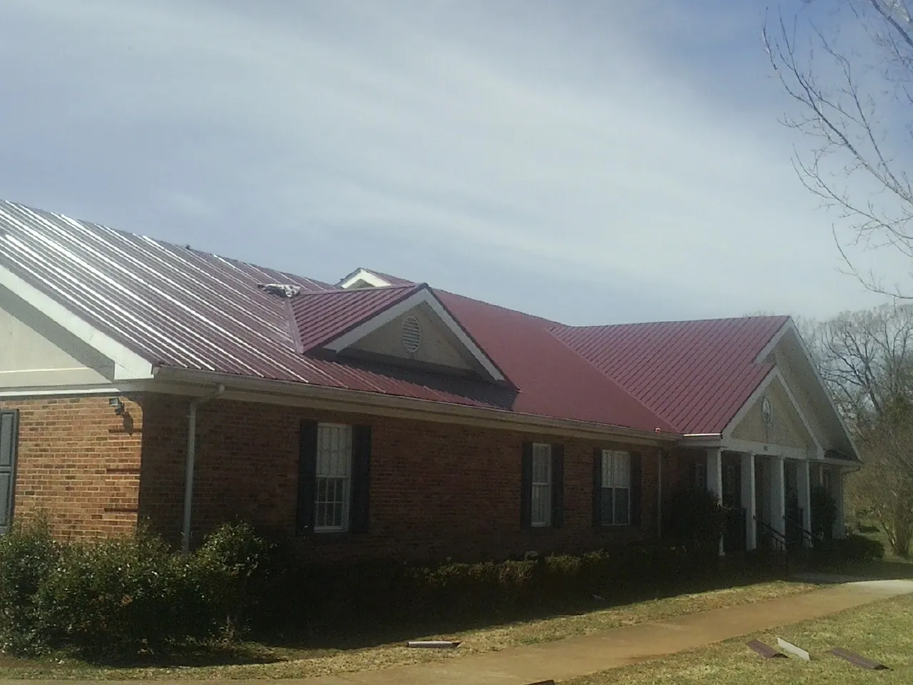 Red metal roof with gabled entries on a long brick building, from a Hail Damage Roof Repair job in Brewerton