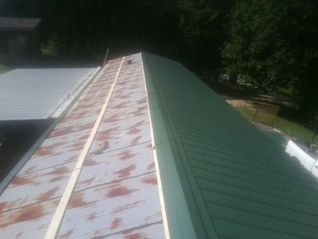 Old rusted panels beside newly installed green metal roofing — Wind Damage Roof Repair by Roofing Brothers in Brewerton