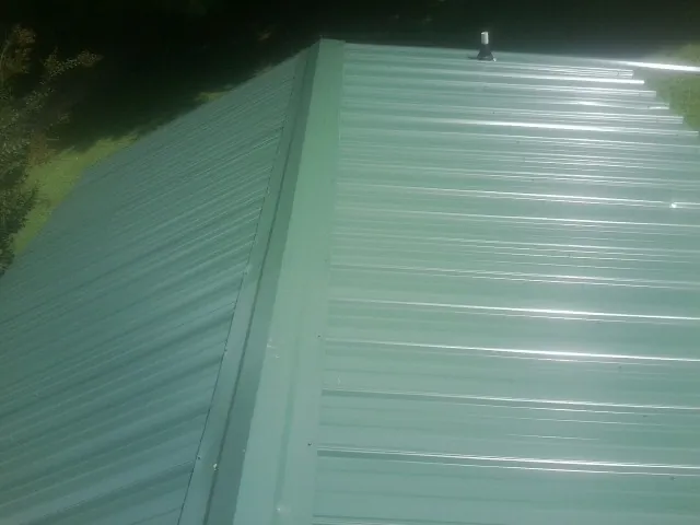 New green metal panels meeting at the ridge of a roof — Flat Roof Repair work by our crew in Brewerton