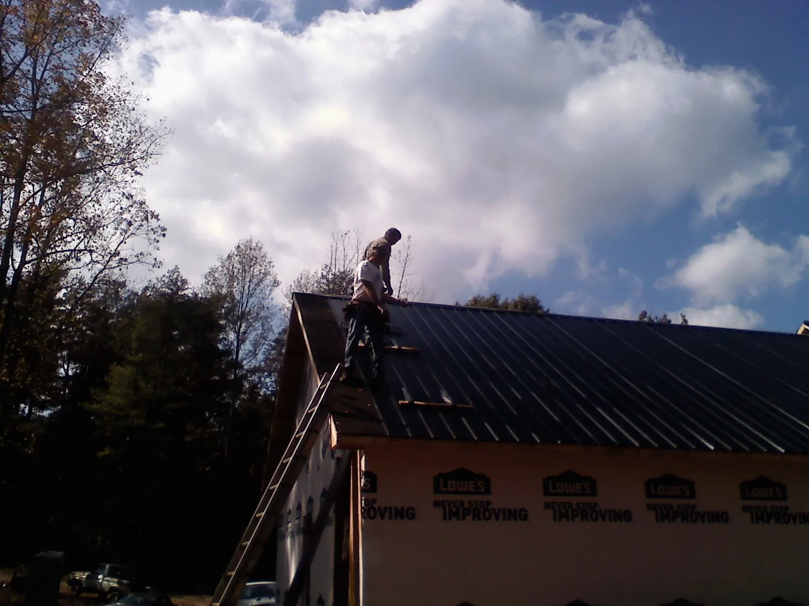 Roofer fastening dark metal panels high against a cloudy sky, from a Roof Inspection job in Brewerton