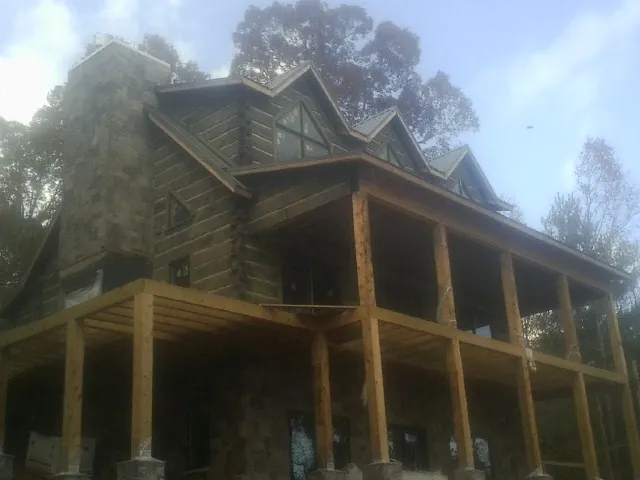 Stone chimney and dormers on a large log home with a timber porch in Brewerton