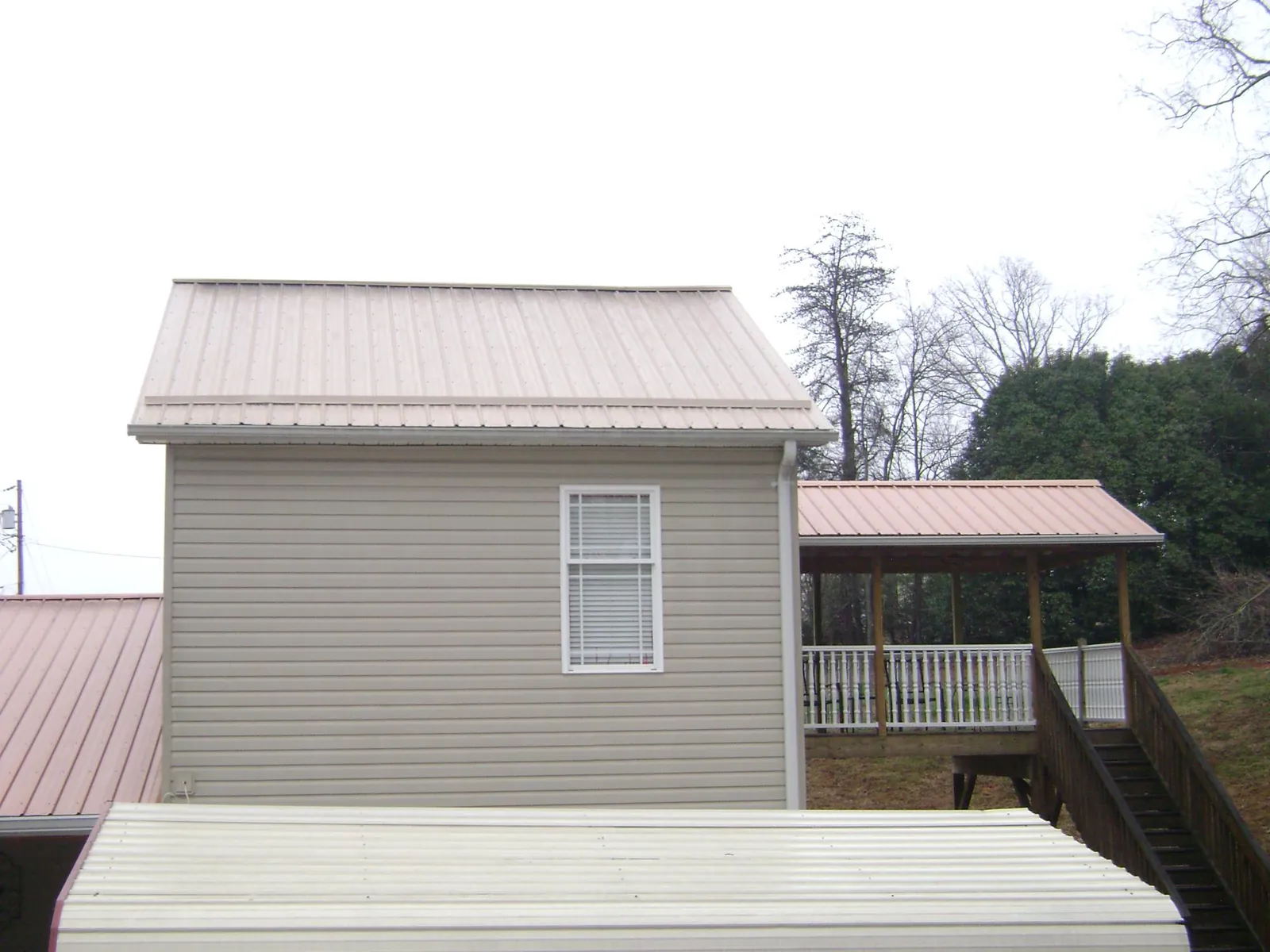 Tan metal roofs on a two story addition and attached porch, from a Roof Replacement job in Brewerton